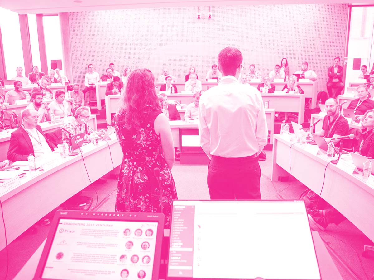 Two founders standing at the front of a large group meeting at a CDL program session.